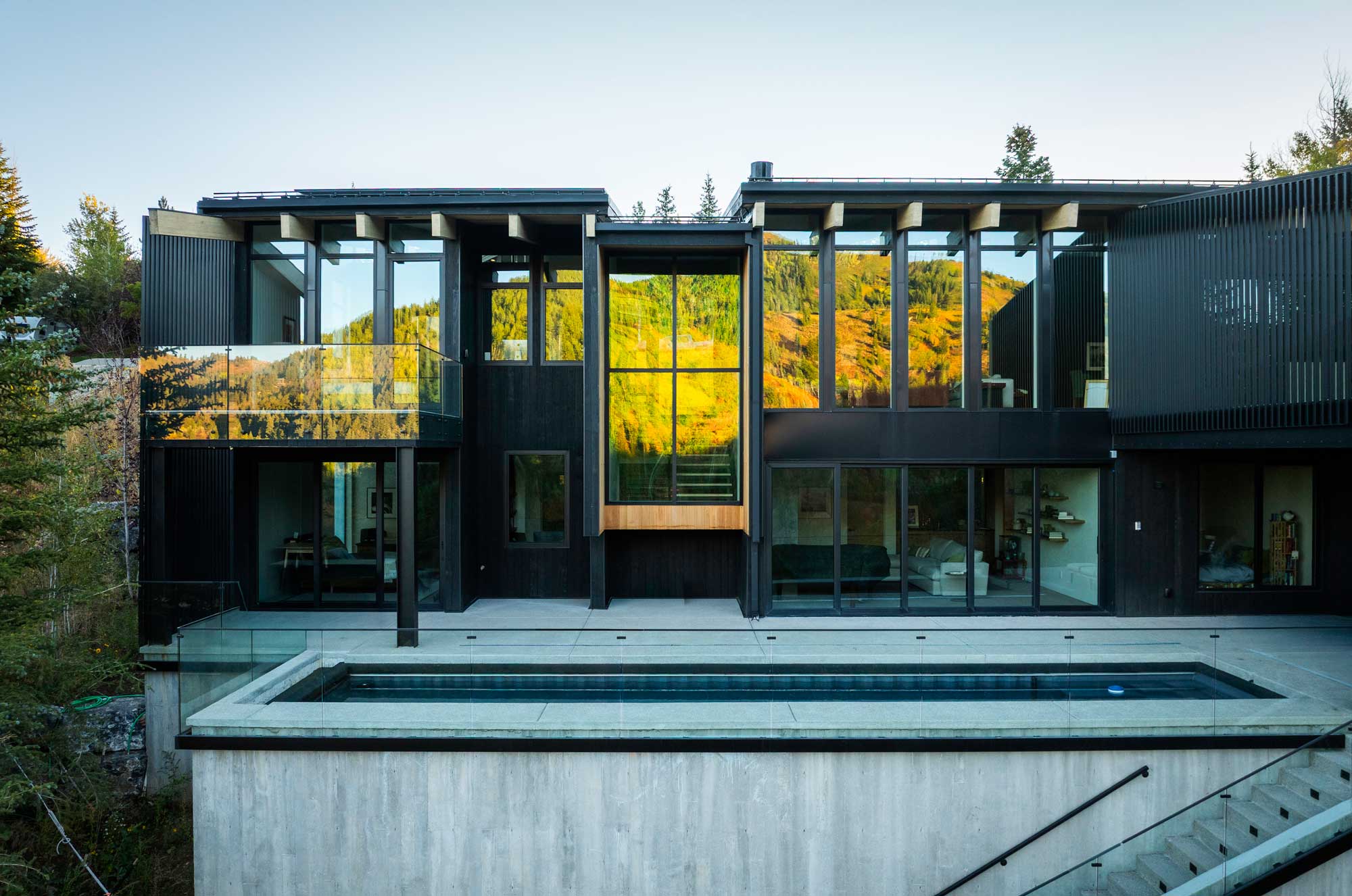 A modern custom home in Park City with expansive floor-to-ceiling windows, dark exterior cladding, and an elevated concrete pool overlooking the surrounding mountain landscape.